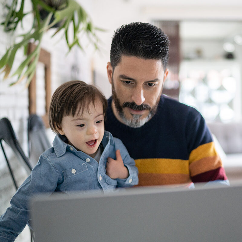 Mature man working at home with baby son - boy with special needs