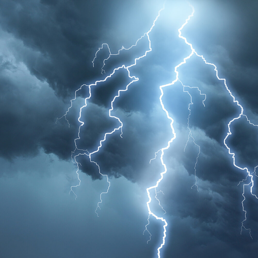 Bright lightning illuminates dark cloudy sky during a thunderstorm. Natural dangers and majestic beauty. Real cloudscape with computer generated lightning. Copy space on image side.